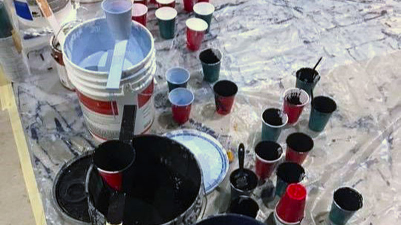Buckets and cups filled with Sporting Blue and black paint sitting on a plastic tarp